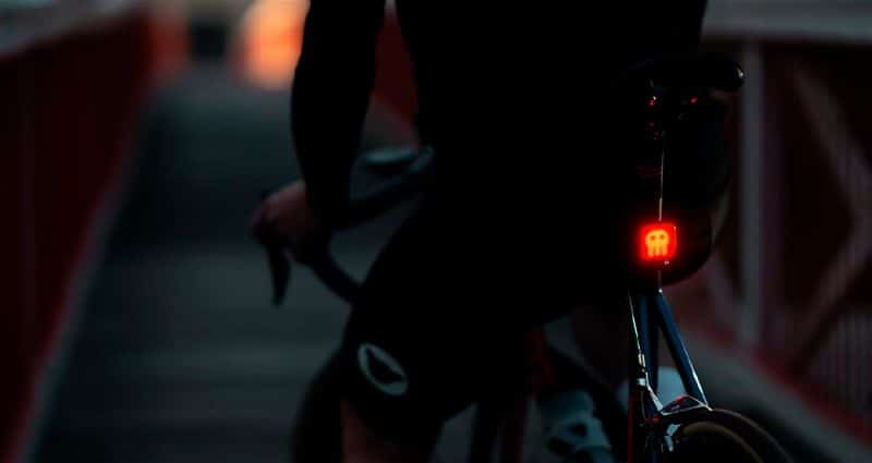 Imagem escura de pessoa sentada em bicicleta virada de costas e iluminação traseira da bicicleta