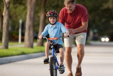 Pai ensinando criança a andar de bicicleta