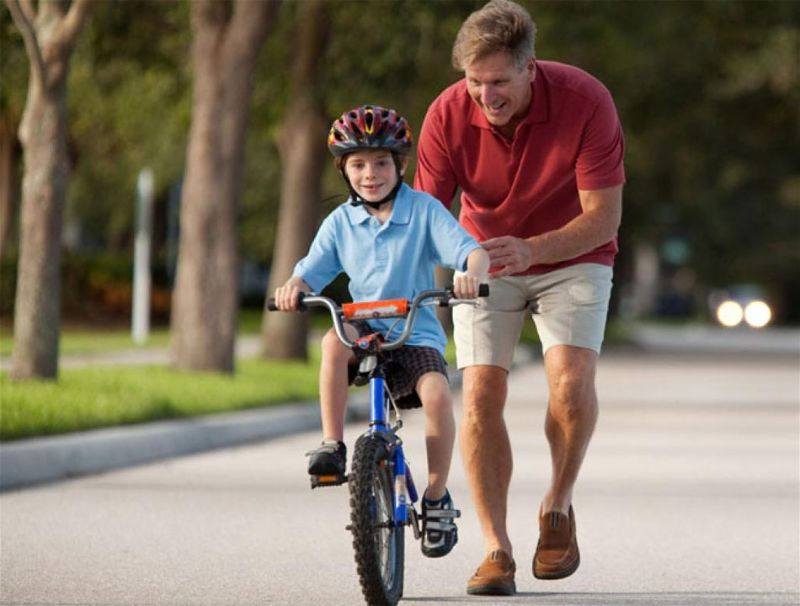 Pai ensinando criança a andar de bicicleta