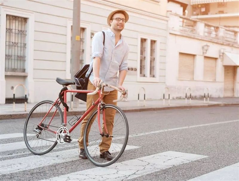 Rapaz em pé segurando bicicleta sobre faixa de pedestre