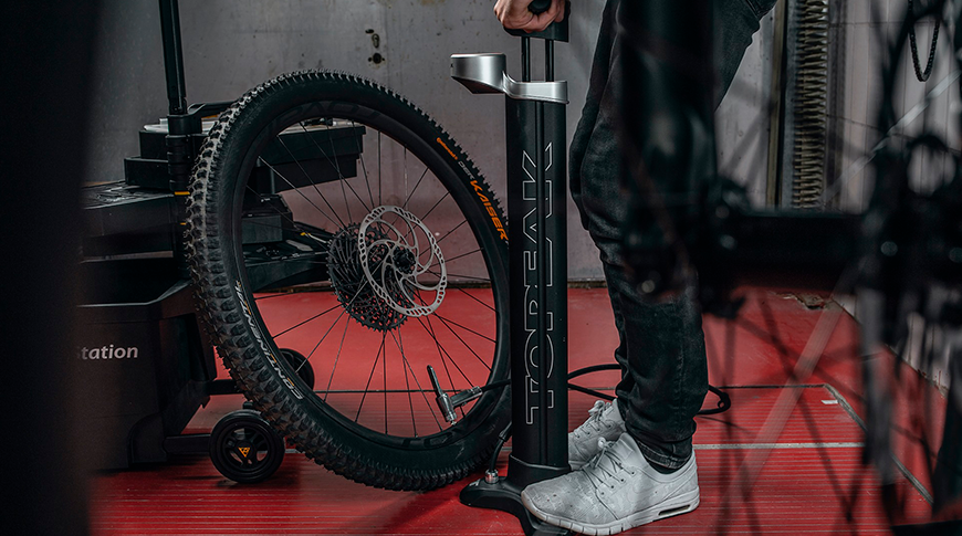 Imagem com uma pessoa enchendo pneu de bicicleta com uma bomba de pé em foco